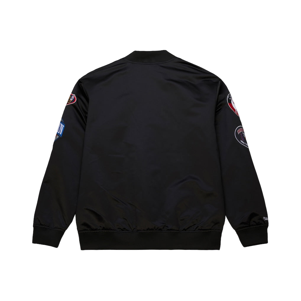 Black bomber jacket with patches on the back against a white background